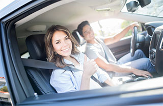 Young couple sitting in a car giving a thumbs up